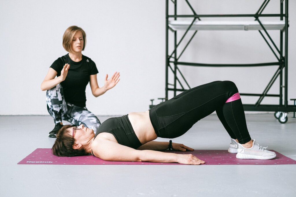 Woman Doing Pelvic Floor Exercise Lying on Purple Yoga Mat with Personal Trainer